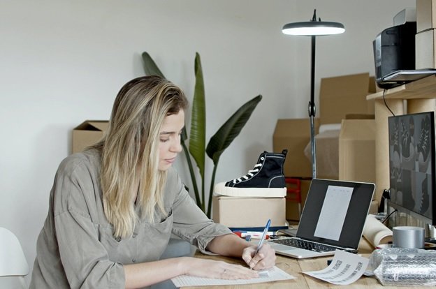 A woman is writing down minimum and maximum prices for her Amazon repricer tool